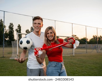 Two soccer fans girl and a guy with soccer ball and scarf standing on soccer field  - Powered by Shutterstock