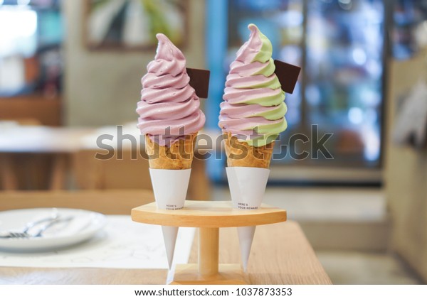 Two soft serve ice cream, sweet potato and melon\
mixed with sweet potato flavours with waffle cone put on wooden ice\
cream stand.