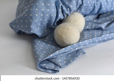 Two Soft White Dryer Balls On A Blue Sheet With White Polka Dots On A White Background