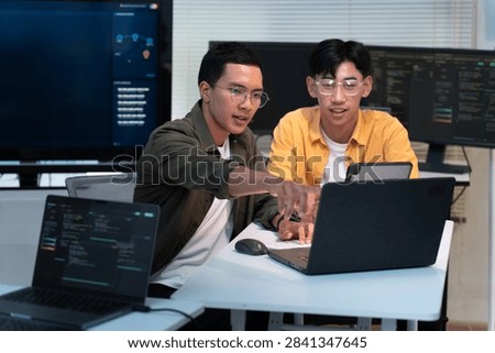 Two software developers collaborate on coding and technical research using laptops in a modern office