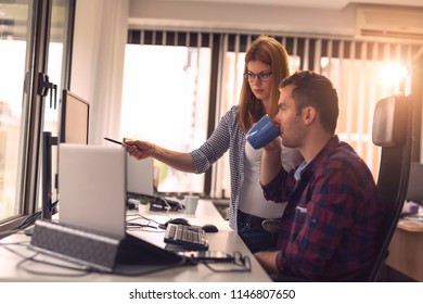 Two software developers working on a new project in a software developing company office. Focus on the woman poiting to the comuter screen