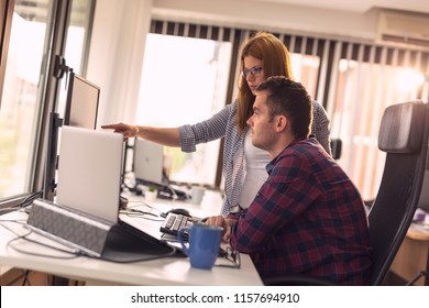 Two software developers working on a new project in a software developing company office. Focus on the woman poiting to the comuter screen