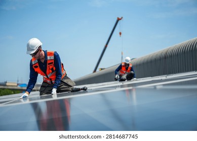 Two solar installation engineers in white helmets and high visibility vests deliberately kneel together at the array edge preparing the next fixings on the curved metal roof.