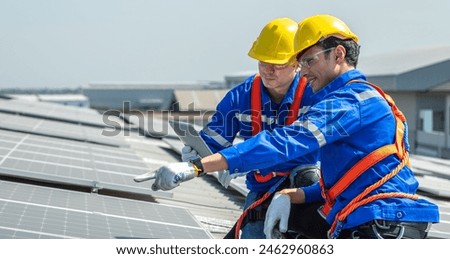 Two solar panel engineers wearing safety gear are inspecting a rooftop solar panel installation.