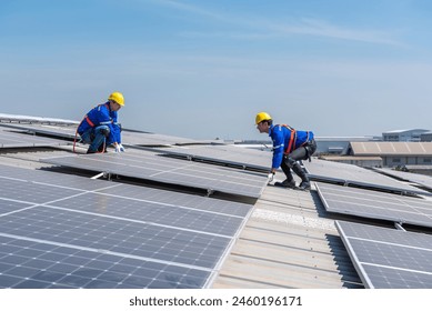 Two solar panel technicians in hard hats and safety gear install solar panels on a commercial building