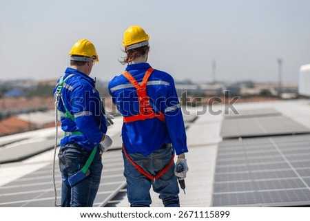 Two solar panel technicians in safety gear inspecting rooftop installation site, representing renewable energy solar power systems, teamwork, clean technology industrial planning and workplace safety.