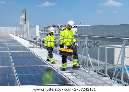 Two solar technicians installing and inspecting photovoltaic panels across a large industrial rooftop solar power system.