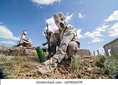 Two Soldiers In The Gas Masks And Protective Clothes Are Testing Biological Weapon On The Ruined Background.