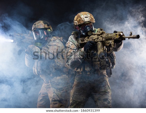 Two soldiers in military gear, bulletproof vests
and gas masks cover each other and raise their submachine guns
taking aim, in full combat readiness to break through the smoke
from chemical weapons