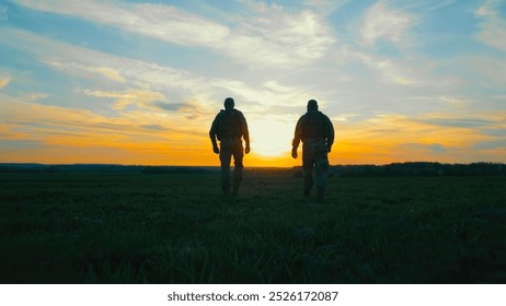 Two soldiers walking across a field at sunset. A dramatic silhouette of two soldiers walking through a field during sunset. - Powered by Shutterstock