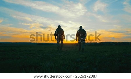 Two soldiers walking across a field at sunset. A dramatic silhouette of two soldiers walking through a field during sunset.