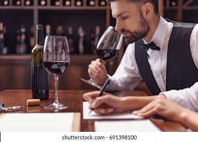 Two sommeliers, male and female tasting red wine and making notes at degustation card