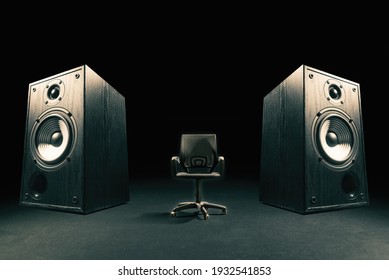 Two sound speakers with office chair between them on black background.