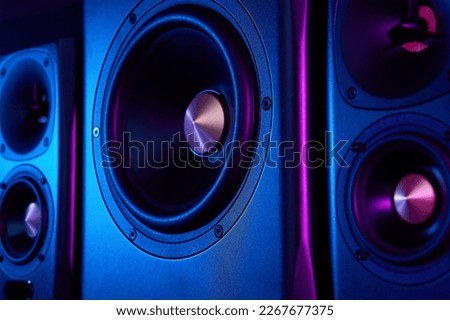 Two sound speakers and subwoofer on dark background with neon lights. Set for listening music. Audio equipment