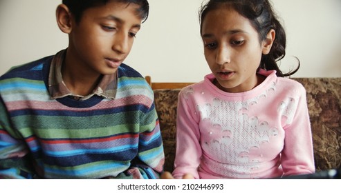 Two South Asian Kids Sitting Together In Front Of A Tablet