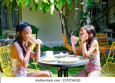 Two Southeast Asian Ethnicity Girls in Swimsuit Having Some Meals and Fun Together After Swimming Activities. Making a Toast. Looking and Smiling. - Powered by Shutterstock