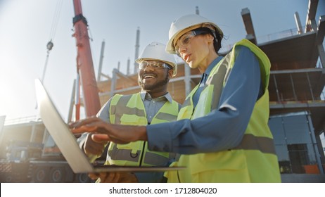 Two Specialists Inspect Commercial  Industrial Building Construction Site  Real Estate Project and Civil Engineer  Investor Use Laptop  In the Background Crane  Skyscraper Concrete Formwork Frames
