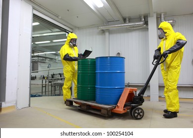 Two specialists in protective uniforms,masks,gloves and boots, dealing with barrels of toxic waste on forklift in factory