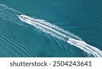 Two speedboats create parallel, foamy trails on a vast turquoise sea, with a small red buoy floating nearby.