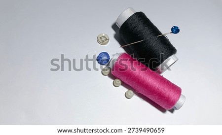 Two spools of sewing thread in black and vibrant pink with a blue-headed pin and assorted buttons. Isolated flat lay on a white background for tailoring and handicraft concepts.
