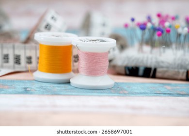Two spools of thread, one yellow and one pink, sit on a crafting table alongside colorful sewing pins and measuring tape, creating an inviting sewing atmosphere during the day.