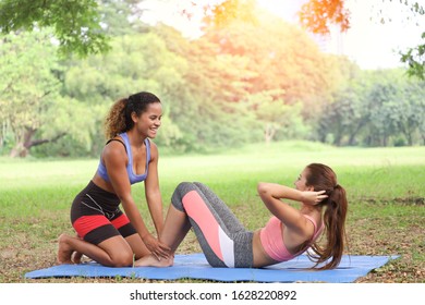 Two sport women exercise and sit up together in a green park - Powered by Shutterstock