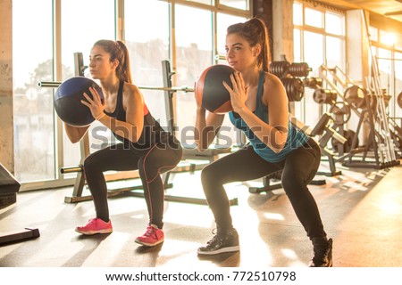 Two sporty girls doing exercises with fitness balls in the gym.