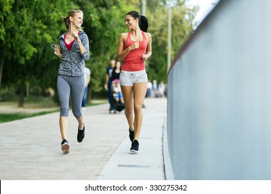 Two Sporty Women Jogging In City While Listening To Music