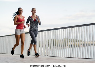 Two Sporty Women Jogging In City While Listening To Music