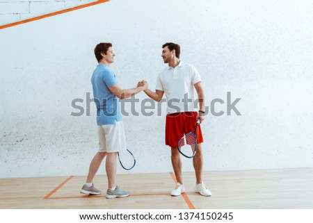 Two squash players with rackets shaking hands and looking at each other