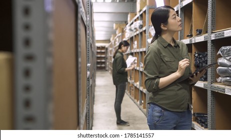 Two Staff Coworkers Counting Products In Box On Shelves And Preparing Invoice. Group Of Young Female People Working Together At Warehouse For Online Seller Business. Lady Colleagues In Stockroom