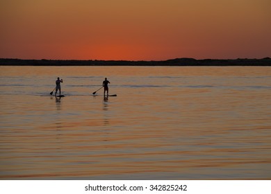 Two Stand up paddlers as silhouettes in the sunset