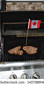 Two Steaks On Barbecue Grill With Canadian Flag In One Steak. Canada Day Celebration