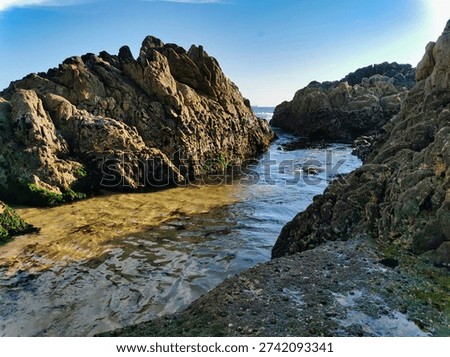 Two steep cliffs with a gap inbetween with sea water rushing in. Pebble beach and blue sky on background.   . Tropical sunset at the beach. Sea and rocks.