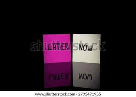 Two sticky notes with words NOW and LATER on dark background with mirror reflection. Concept of procrastination, priority, decision and time management.