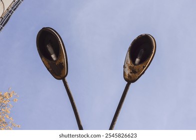 Two street lights are leaning on a pole. The lights are old and rusted. The sky is clear and blue - Powered by Shutterstock