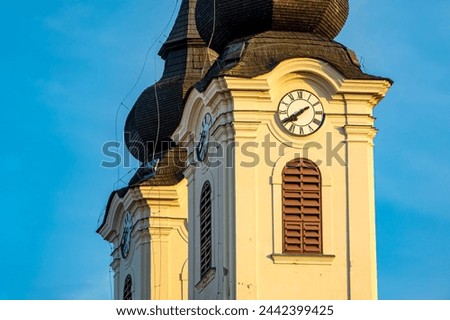 The two striking towers with bell windows and tower clocks of Tiahany Monastery in oblique view in the evening or morning sunlight under a cloudless blue sky