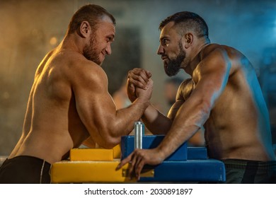 Two strong athletes in the gym compete in arm wrestling. Bodybuilders armwreslers in athletic training room