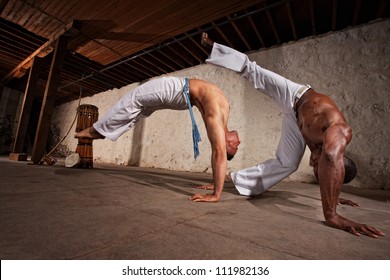 Two strong male capoeira experts fighting indoors