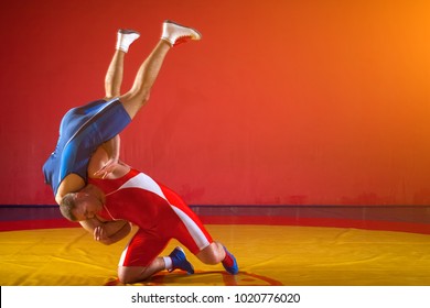 Two strong wrestlers in blue and red wrestling tights  making a hip throw  on a yellow wrestling carpet in the gym. Young man doing grapple.