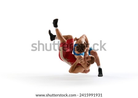 Two strong wrestlers in blue and red wrestling uniform fighting and making hip throw in motion against white studio background. Concept of fair wrestling, championship, win competition.