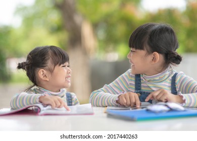 Two student little Asian girls reading the book on table
