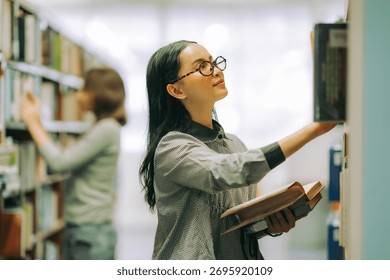 Two Student researching reference books in academic library, highlighting education, learning motivation, and scientific discovery. Woman choosing book on shelf collection.