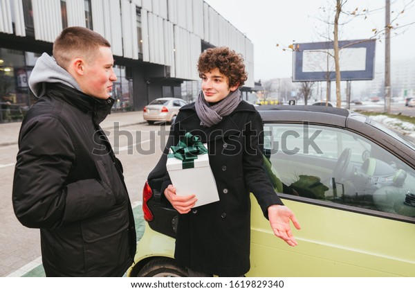 Two\
student youth men in black coats meeting with shopping mall on\
background. Teenage boy advice with friend about gift for\
girlfriend or mother. Holidays Clutter\
Concept.