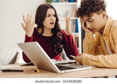 Two students arguing during a study session, surrounded by a laptop and notebook on the desk, highlighting conflict and frustration