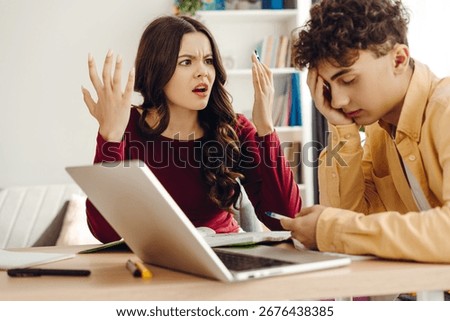 Two students arguing during a study session, surrounded by a laptop and notebook on the desk, highlighting conflict and frustration