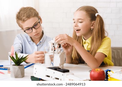 Two students, a boy and a girl, work together on a science project in a classroom setting. The boy is wearing glasses and is focused on robot - Powered by Shutterstock