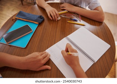 Two students collaborate on a study project at a round wooden table, with notebooks, pens, and a smartphone scattered around. They focus on learning and homework tasks, emphasizing teamwork. - Powered by Shutterstock