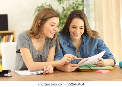 Two students doing homework together and helping each other sitting in a table at home with a homey background