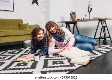 Two students doing homework together and helping each other lying on the floor at home with a homey background